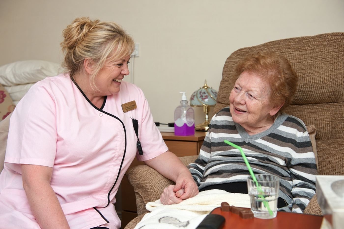 A carer holding a resident’s hand as they talk in her room.