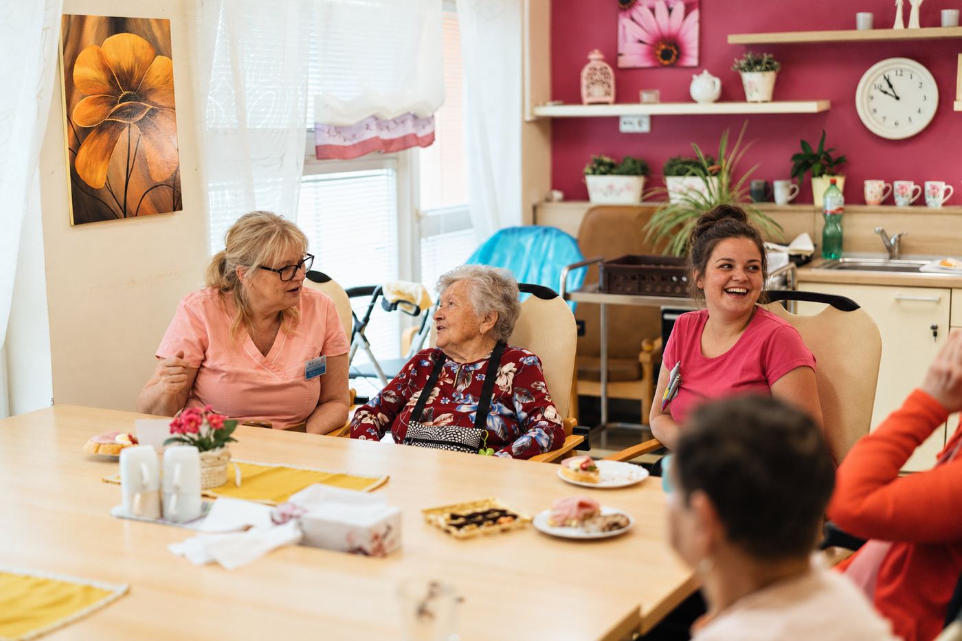 Residents and staff sitting around a table with tea and cakes, laughing together.